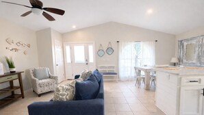 Un salon spacieux avec un canapé bleu, un fauteuil à motifs et un coin repas comprenant une table et des chaises blanches.