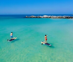 Two people paddleboarding in clear turquoise water with a rocky breakwater in the background. - 2 Minutes Toes in Sand - Beach - Emerald Waters - Sunsets - Lagoon  (Panama City Beach)