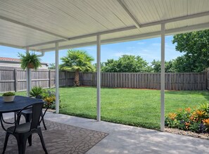 A covered patio area with a table and chairs, a small garden, and a wooden fence in the background.