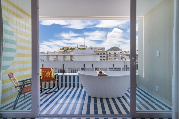 A modern bathroom with a freestanding bathtub, a chair, and a view of the cityscape through a glass door.