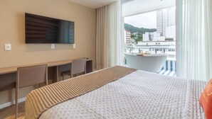 Ein Hotelzimmer mit Bett, Schreibtisch, zwei Stühlen, Fernseher und einem Balkon mit Blick auf Gebäude.