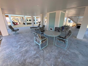 An outdoor patio area with a round table and four chairs, surrounded by a concrete floor and white pillars. - Nautical Nest - Quick Walk to Beach (Fort Myers Beach)