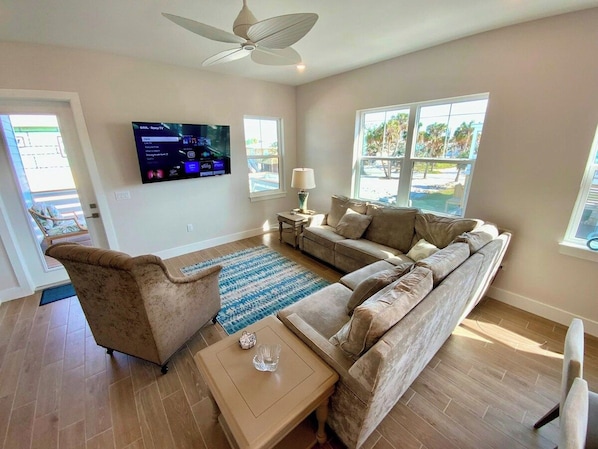 Una sala de estar con sofá, sillón, mesa de centro, televisión y ventanas.