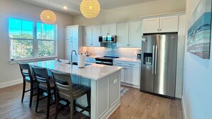 Una cocina moderna con gabinetes blancos, electrodomésticos de acero inoxidable y una isla grande con taburetes de bar.