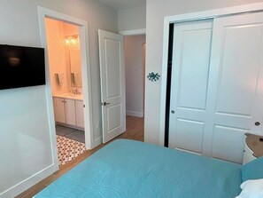 A bedroom with a bed, a TV mounted on the wall, and a bathroom visible through an open door. - Nautical Nest - Quick Walk to Beach (Fort Myers Beach)