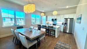 Una cocina moderna con armarios blancos, electrodomésticos de acero inoxidable y una zona de comedor con mesa y sillas de madera.