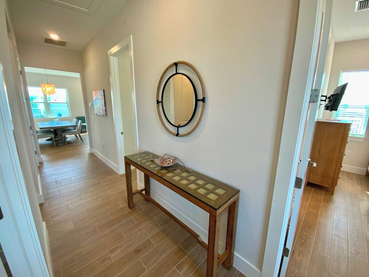 A hallway with a glass-top console table, a round mirror on the wall, and a wooden door leading to another room.
