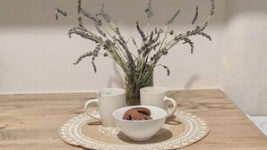 A kitchen counter with a wooden surface, a white mug, a white bowl with cookies, and a small potted plant with lavender.
