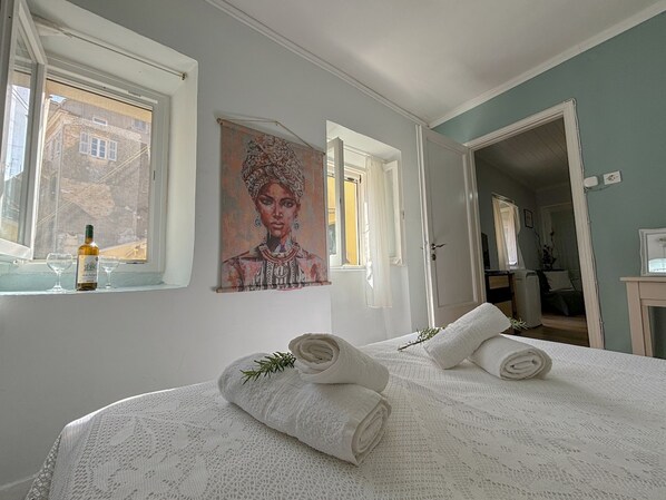 A bedroom with a bed, two rolled towels, a painting, and a bottle of wine on the windowsill. - Amonte - Old Town Centre (Corfu)