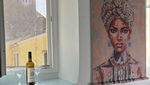 A room with a large window, a bottle of wine, and a painting on the wall.