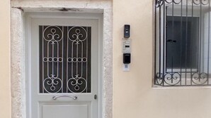 A white door with a decorative metal grille, a small window with a metal grill, and a stone-paved entrance.