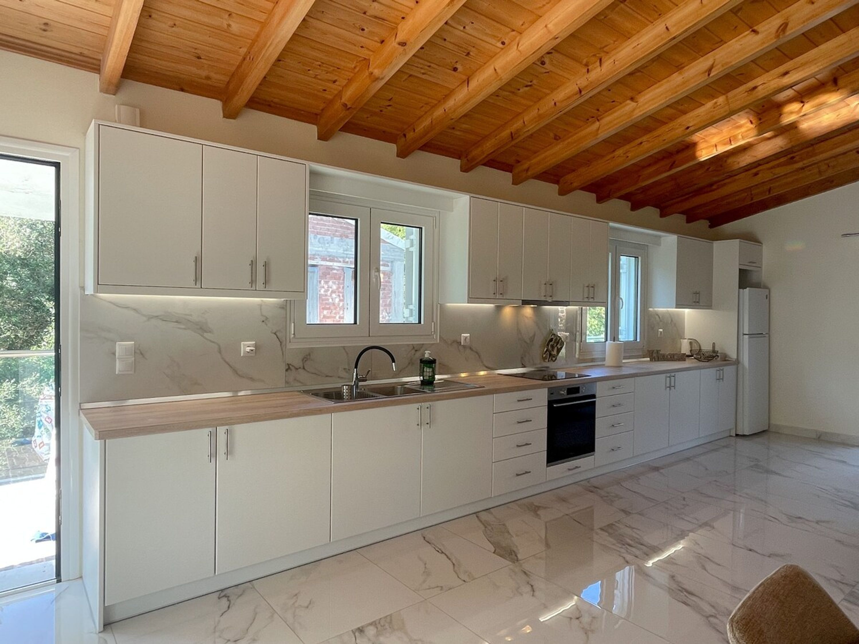 A modern kitchen with white cabinets, a marble countertop, and a wooden ceiling.