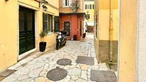 A narrow cobblestone street flanked by yellow buildings with green shutters and a scooter parked in front. - Kukuvayia s Nest-centre Old Town Corfu (Corfu)