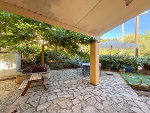Eine Terrassengestaltung mit Steinboden, einer Holzbank und einem Tisch mit Stühlen.