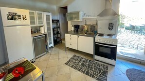 A compact kitchen with a refrigerator, stove, and cabinets. There is a small dining area with a table and chairs. - Ourano -gastouri Village Center (Corfu)