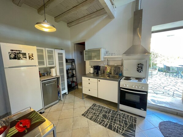 A compact kitchen with a refrigerator, stove, and cabinets. There is a small dining area with a table and chairs. - Ourano -gastouri Village Center (Corfu)