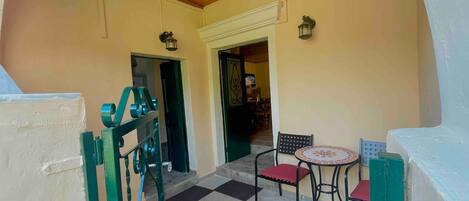 A covered outdoor seating area with a table and chairs, a metal gate, and a door leading to an interior space.
