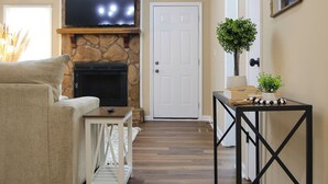 A living room with a fireplace, a television mounted above it, a sofa, and a small table with decorative items. - Charming 3-bedroom home in Fayetteville: 5 min from Base (Fayetteville)