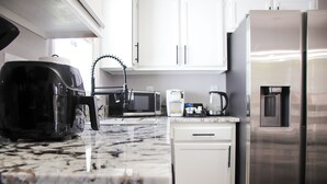 A kitchen with white cabinets, a stainless steel refrigerator, a coffee maker, and a microwave. - Charming 3-bedroom home in Fayetteville: 5 min from Base (Fayetteville)