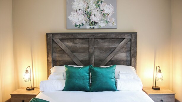A bedroom with a wooden headboard, white bedding, teal pillows, and two bedside lamps. - Charming 3-bedroom home in Fayetteville: 5 min from Base (Fayetteville)
