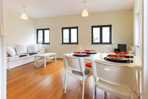 Relax in a spacious living area with a sofa, coffee table, and dining space for two, offering a view of the outdoors.