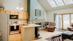 A spacious kitchen with wooden cabinets, a stone fireplace, and a large window. - Ski-In/Ski-Out Townhouse at Tenney Mountain Resort (Plymouth)