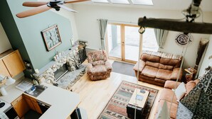 A cozy living room with a stone fireplace, a sofa, a chair, and a dining area with a kitchen counter. - Ski-In/Ski-Out Townhouse at Tenney Mountain Resort (Plymouth)