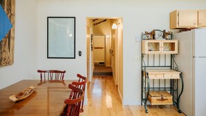A dining area with a wooden table and chairs, a kitchen with cabinets and a refrigerator, and a hallway leading to another room. - Ski-In/Ski-Out Townhouse at Tenney Mountain Resort (Plymouth)