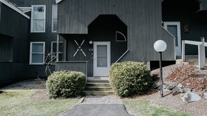 A modern two-story building with a dark exterior, a front door, and a unique architectural feature resembling a cross. - Ski-In/Ski-Out Townhouse at Tenney Mountain Resort (Plymouth)