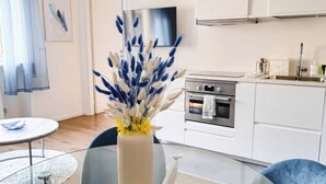 A modern kitchen with white cabinets, a stainless steel oven, and a sink. There is a glass dining table with blue chairs and a vase with blue and white flowers. - Morgagni Suites (Bologna)