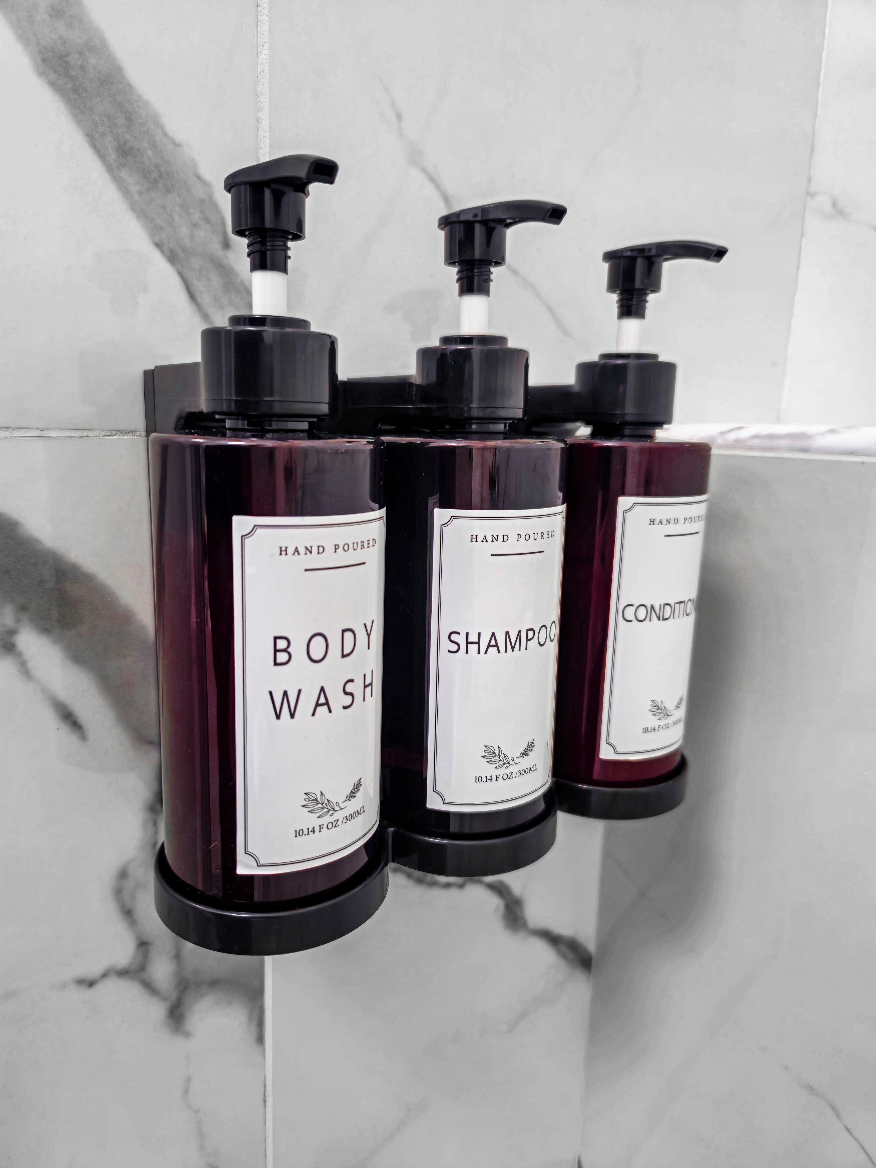 Tre flaconi di bagnoschiuma, shampoo e balsamo versati a mano su un muro di marmo.