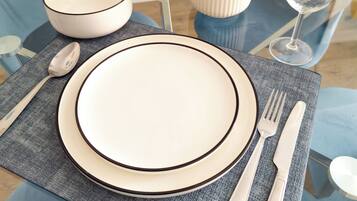 A dining table set with a white plate, bowl, cutlery, and a vase with yellow flowers.