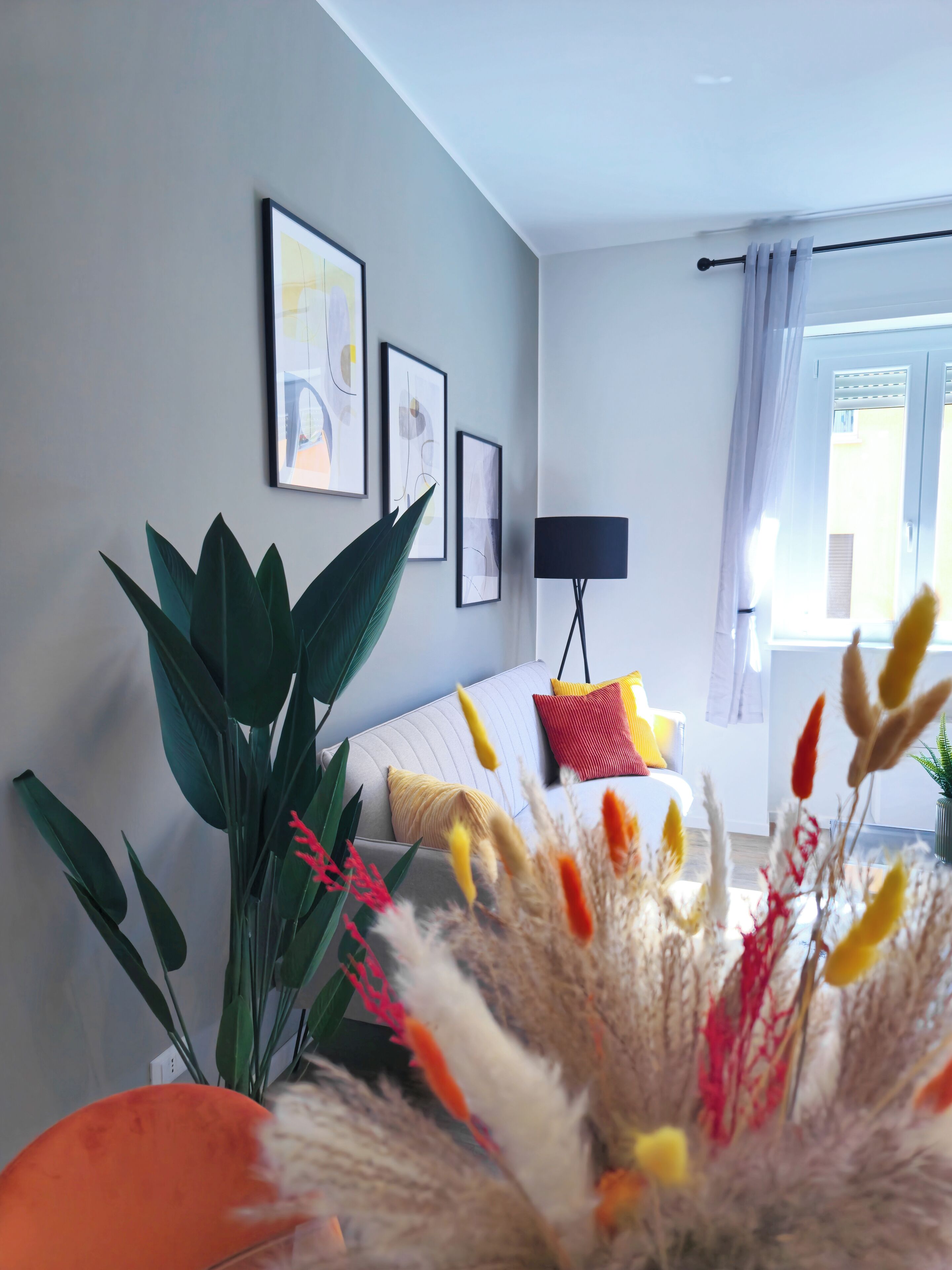 A modern living room with a sofa, a floor lamp, and a large plant.