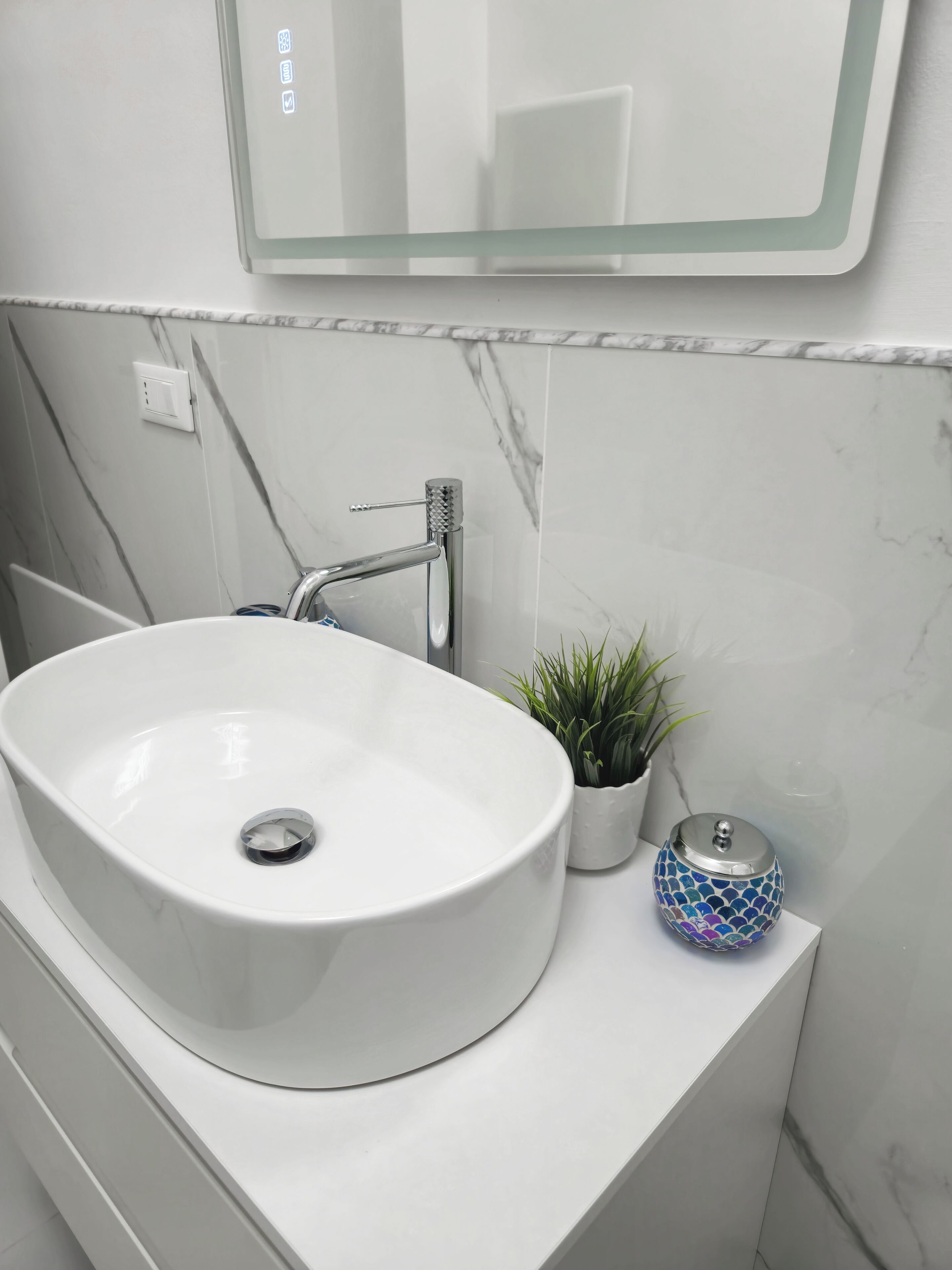 A bathroom with a white sink, a mirror, and a small potted plant.