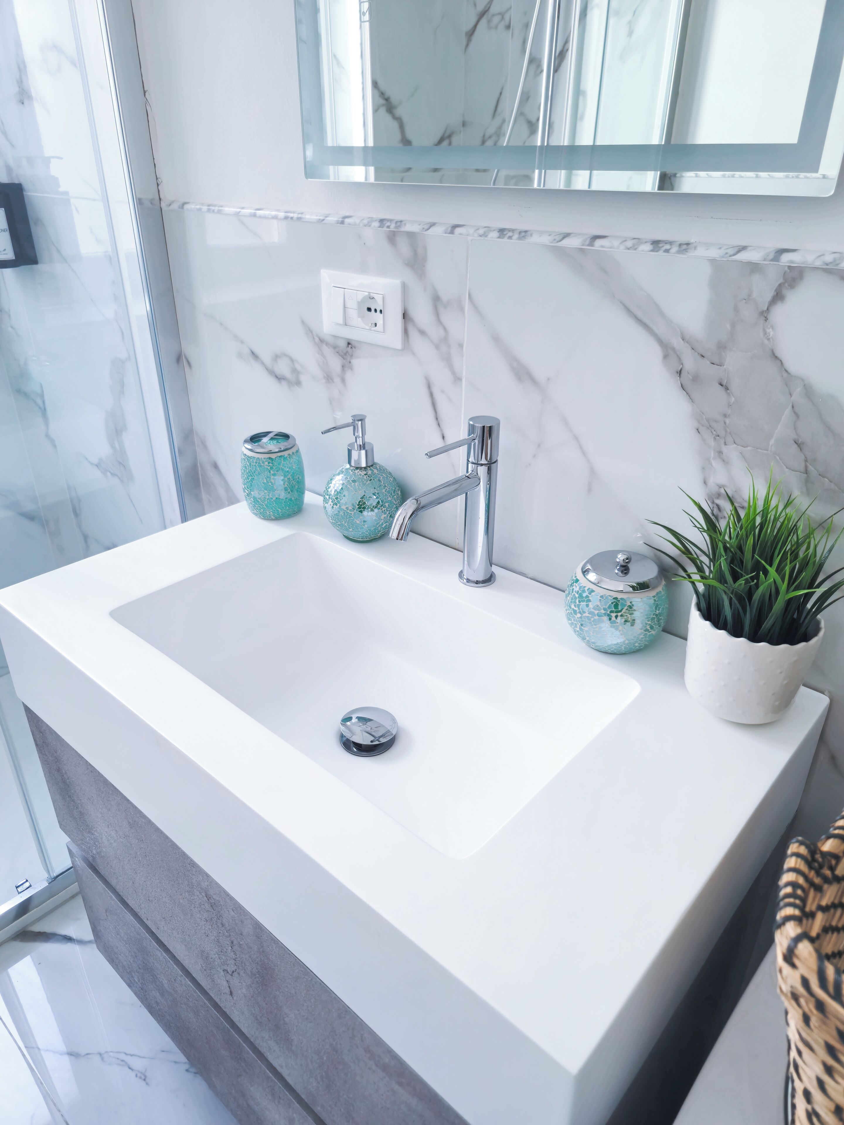 A bathroom with a white sink, a mirror, and a marble wall.