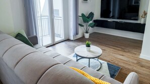 A modern living room with a grey sofa, a coffee table with a plant, a flat-screen TV, and a balcony with a railing. - Morgagni Suites (Bologna)