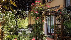 A garden with a wooden pergola, a white table and chairs, and a building with a brown door. - Rose Corner House (Orvieto)