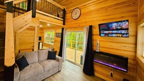 L’intérieur chaleureux d’un chalet avec un escalier en bois, un canapé, une cheminée et un téléviseur diffusant Netflix.