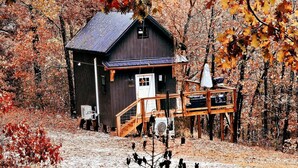 Un chalet rustique doté d’une terrasse en bois, entouré d’un feuillage automnal.