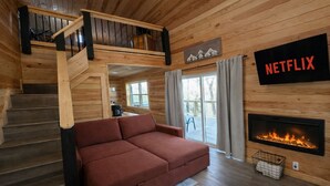 L’intérieur d’un chalet chaleureux, avec un escalier en bois, un canapé, une cheminée et le logo de Netflix.