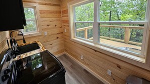 L’intérieur d’une cabane avec des murs en bois, une grande fenêtre donnant sur une terrasse et un poêle noir.