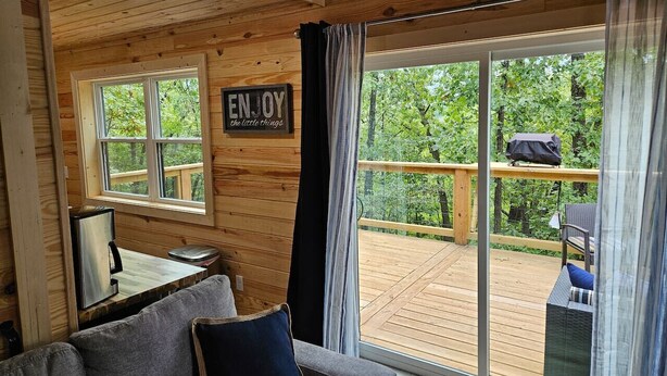 L’intérieur chaleureux d’un chalet avec un plafond en bois, un canapé, une table basse et une grande fenêtre donnant sur une terrasse.