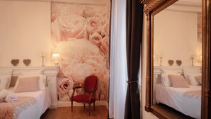 Une chambre d’hôtel avec deux lits, un fauteuil rouge, un grand papier peint à motifs floraux et un miroir.