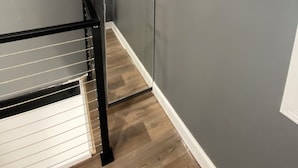Een gang met een houten vloer, een zwarte balustrade en grijze muren.