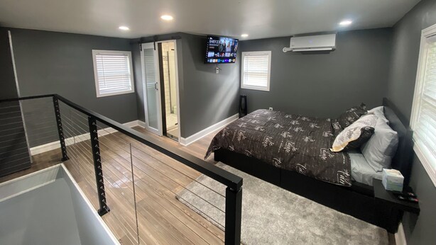 Een slaapkamer met een bed, een aan de muur bevestigde televisie en een raam met zonwering.