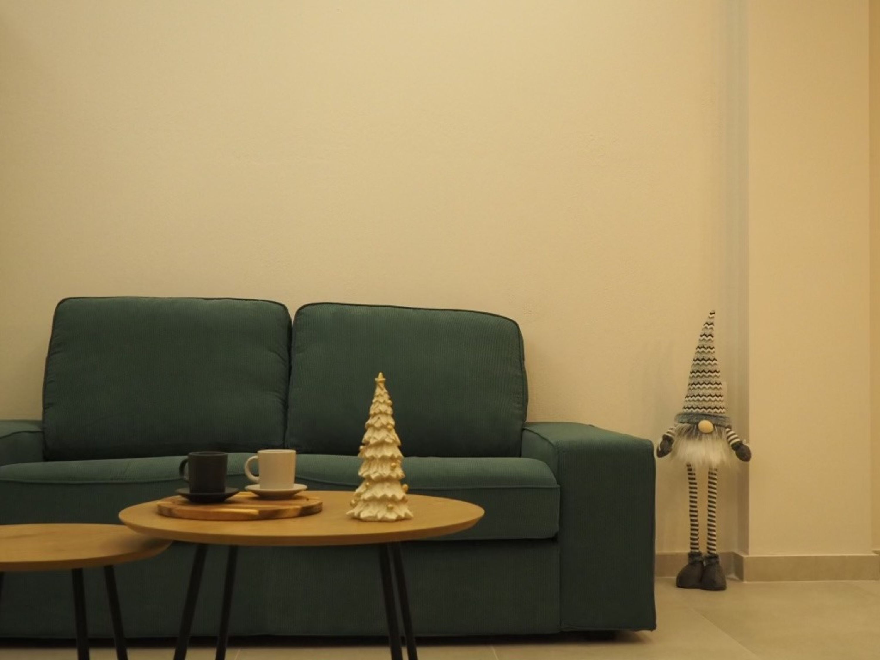 A green sofa, a small round table with a white cup and saucer, and a decorative Christmas tree.
