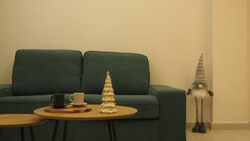 A green sofa, a small round table with a white cup and saucer, and a decorative Christmas tree.