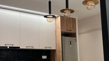 A modern kitchen with white cabinets, a wooden accent wall, and a marble countertop. There is a dining area with a wooden table and chairs.