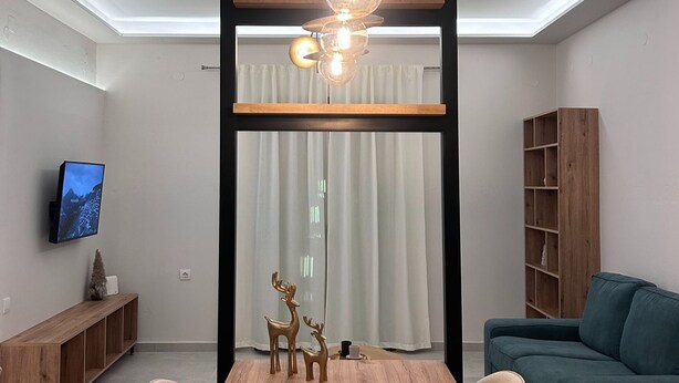 A modern dining area with a wooden table, chairs, a chandelier, and a television on the wall. - Abete Luxury Apartments (Metsovo)