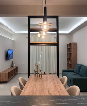Un'area pranzo moderna con un tavolo in legno, sedie, un lampadario e un televisore a parete.